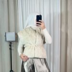 Gilet sans manches en fausse fourrure blanche porté avec jupe satinée.