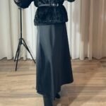 Jupe longue satinée noire fluide portée avec un gilet noir