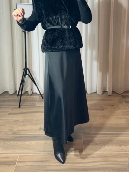 Jupe longue satinée noire fluide portée avec un gilet noir