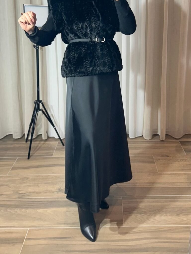Jupe longue satinée noire fluide portée avec un gilet noir