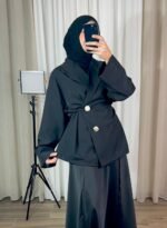 Veste noire croisée avec boutons bijoux dorés portée en tenue élégante