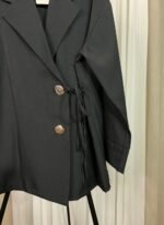 Détail des boutons dorés et du nœud latéral sur une veste noire élégante