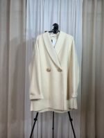 Manteau oversize crème avec boutons dorés suspendu sur un cintre — Mesdames Akbelles