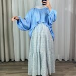 Jupe longue bohème à volants avec motif petites fleurs bleu ciel et jaune, portée avec une blouse fluide bleue et un hijab clair.