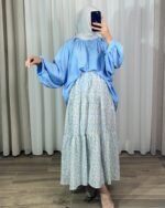 Jupe longue bohème à volants avec motif petites fleurs bleu ciel et jaune, portée avec une blouse fluide bleue et un hijab clair.