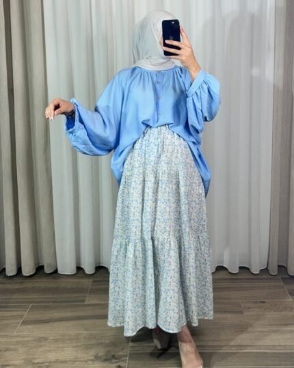 Jupe longue bohème à volants avec motif petites fleurs bleu ciel et jaune, portée avec une blouse fluide bleue et un hijab clair.