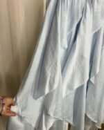 Gros plan sur le tissu fluide plissé et les détails des motifs floraux bleus et jaunes de la jupe.