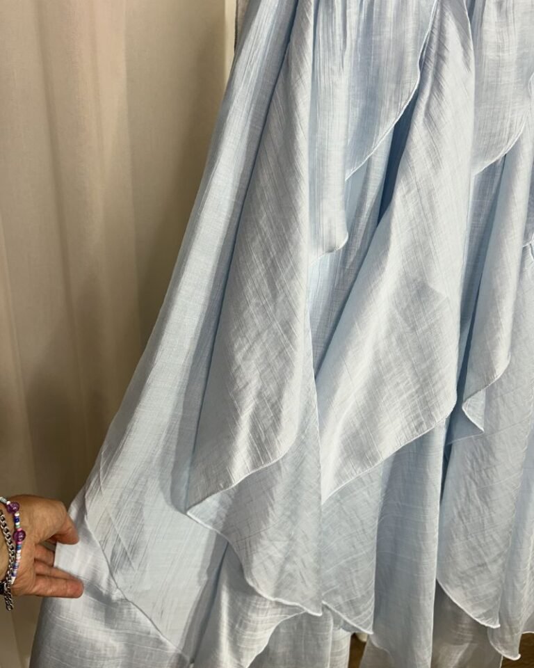 Gros plan sur le tissu fluide plissé et les détails des motifs floraux bleus et jaunes de la jupe.