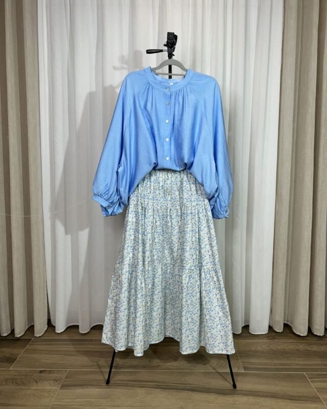 Ensemble assorti composé d'une jupe longue fleurie à étages et d'une blouse fluide bleu azur présentée sur cintre.