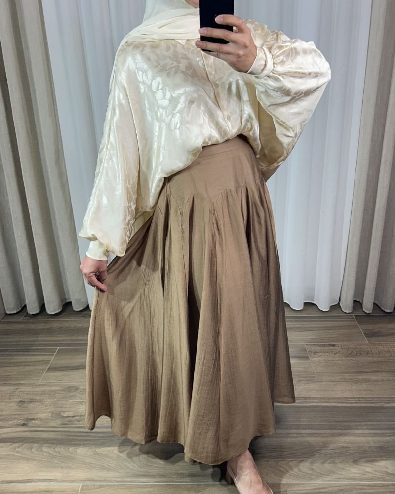 jupe-longue-plissee-fluide-marron Jupe longue plissée fluide de couleur marron avec coupe évasée à volants cascade, portée avec un hijab blanc.