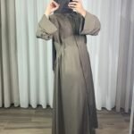 Robe longue style chemise couleur taupe avec manches longues évasées, portée de profil.