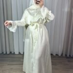Robe longue style chemise couleur crème pastel avec motifs fins, ceinture nouée à la taille et poignets à volants cascade.