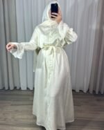Robe longue style chemise couleur crème pastel avec motifs fins, ceinture nouée à la taille et poignets à volants cascade.