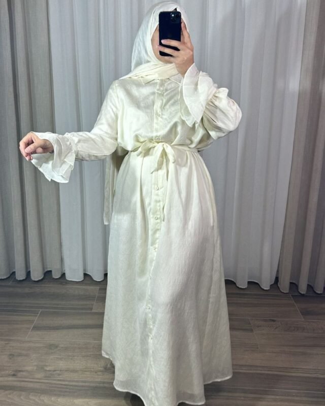 Robe longue style chemise couleur crème pastel avec motifs fins, ceinture nouée à la taille et poignets à volants cascade.