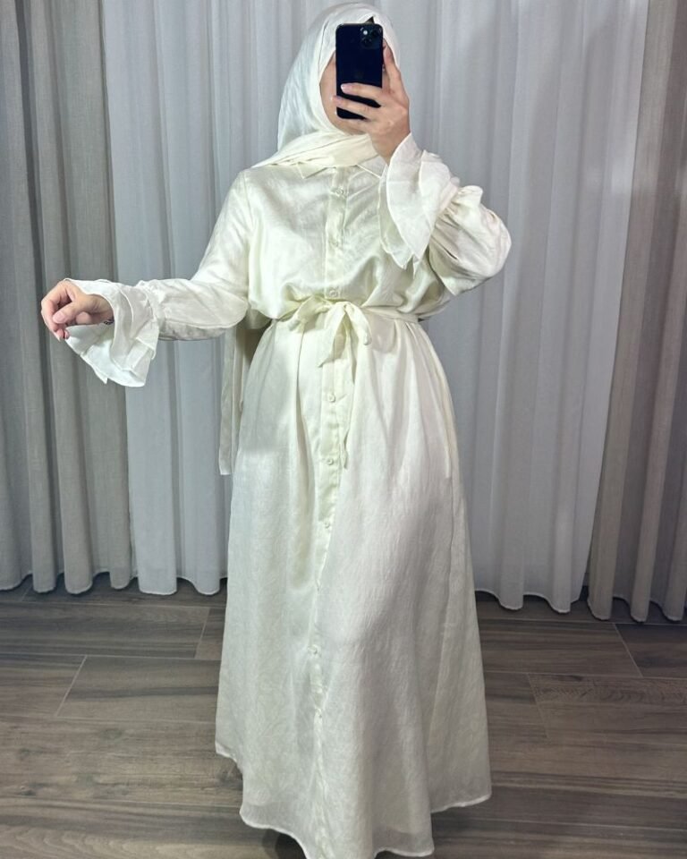Robe longue style chemise couleur crème pastel avec motifs fins, ceinture nouée à la taille et poignets à volants cascade.