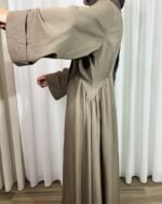 Zoom de profil sur les fronces à la taille et les manches évasées d'une robe longue fluide taupe.