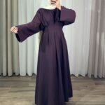 Robe longue élégante couleur aubergine avec manches évasées et taille plissée, portée avec un hijab blanc.