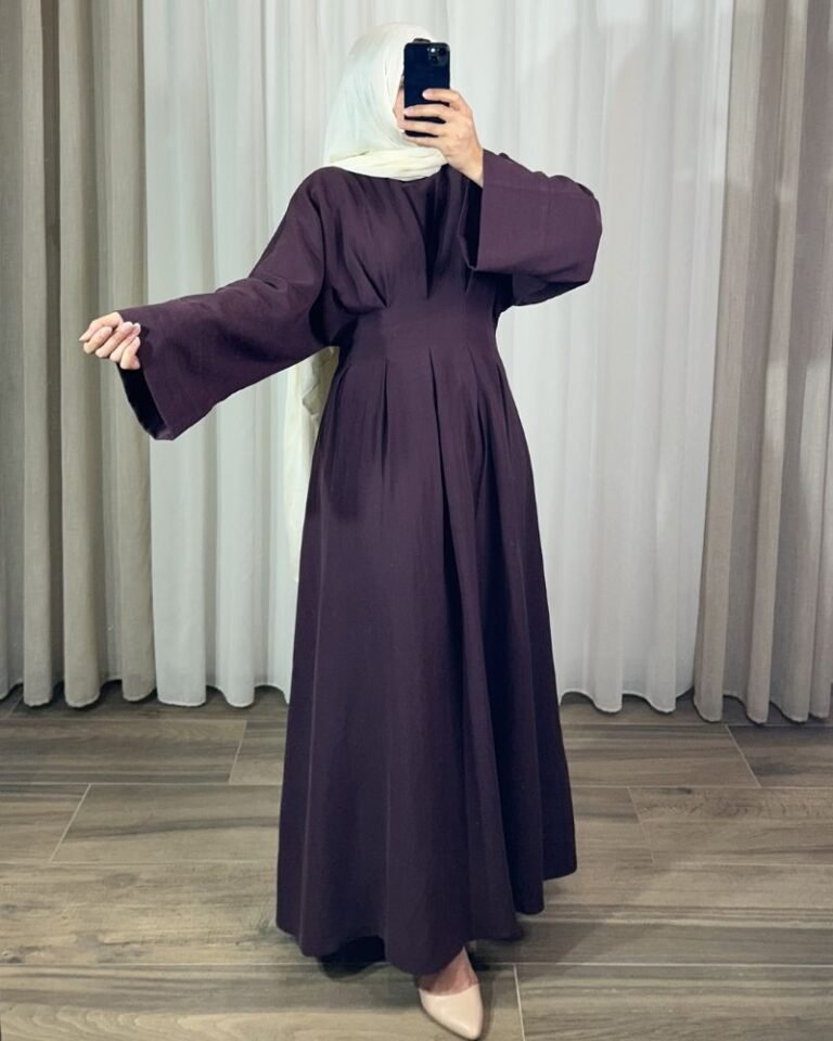 Robe longue élégante couleur aubergine avec manches évasées et taille plissée, portée avec un hijab blanc.