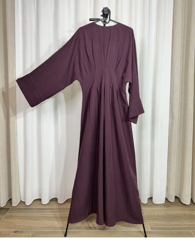 Robe longue de couleur aubergine foncée sur cintre, montrant les détails des plis à la taille et la coupe évasée.